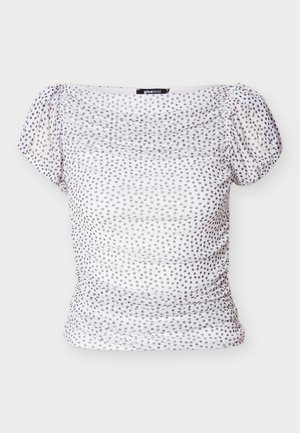 Fehér váll nélküli felső világos lila pöttyökkel. Az elején összegyűrt anyag és a rövid, pufi ujjú kialakítás feszes sziluettet kölcsönöz.