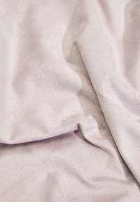 Texturovaná látka v měkkém, světlém růžovém odstínu, zavěšená s jemnými záhyby a hladkým, hedvábným vzhledem. Žádné viditelné vzory nebo kovové detaily.