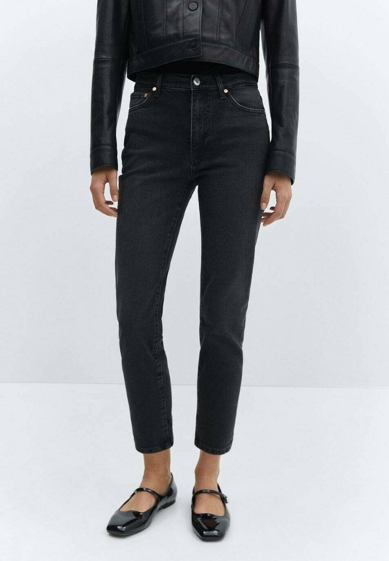 Femme portant un jean droit noir court, une veste courte en cuir noir et des chaussures Mary Jane en cuir verni noir.