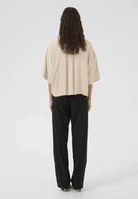 Bé�žová oversized blúzka s krátkymi rukávmi, s prekladaným detailom na chrbte, skombinovaná s čiernymi nohavicami s vysokým pásom. Hladká tkanina a voľný strih.