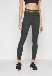 Aukštos talijos, priglundantys leggingai tamsiai žalia spalva, su juodu juosmens kraštu ir geltonu "new balance" prekės ženklu. Sklandus, ištempiamas audinys.