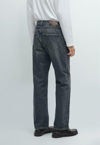 Jeans in denim scuro con un design a gamba dritta, dotati di tasche a pattina posteriori e un'etichetta in pelle sul passante della vita.