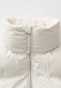 Giacca a vento con collo alto. Esterno crema, morbida fodera in fleece all'altezza del collo, zip centrale e un'etichetta con la scritta "OPUS".