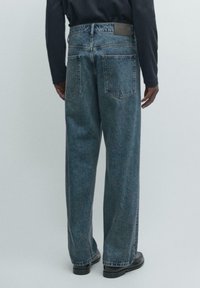 Niebieskie dżinsy z denimu o luźnym kroju, wysokim stanie, pięciokieszeniowym designie i subtelnym spraniu. Z tyłu na pasku znajduje się czarna skórzana naszywka.