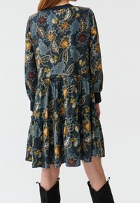 Vestido floral azul marino con diseño en capas, que presenta patrones en dorado, azul y blanco. Mangas largas y puños elásticos, confeccionado con tejido ligero.