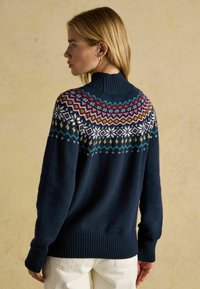 Marineblauer Strickpullover mit hohem Kragen und buntem Fair-Isle-Muster über den Schultern. Gerippte Bündchen und Saum, weiche Textur.