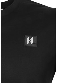 Czarny bawełniany T-shirt z okrągłym dekoltem i teksturowaną prostokątną naszywką z logo z srebrnymi akcentami na piersi.