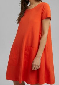 Kortärmad, orange bomullsklänning med lös passform, rund halsringning och två framfickor för extra detalj.