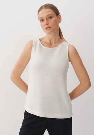 Haut sans manches blanc avec un motif tricoté texturé, col rond et coupe décontractée, associé à un pantalon noir pour le contraste.