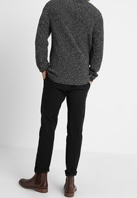 Schwarze, figurbetonte Hose kombiniert mit einem strukturierten, grauen Langarmshirt und braunen Knöchelstiefeln. Das Outfit hat ein lässiges Design.