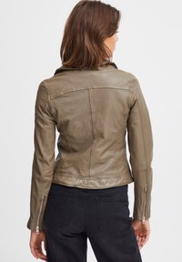 Olive green leather jacket with a fitted design, zippered cuffs, and a smooth texture. Exposed stitching and shoulder seams add detail.