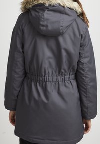 Parka isolée grise avec capuche dotée d'une bordure en fausse fourrure, taille élastique et manches longues. Le tissu est lisse avec une finition mate.