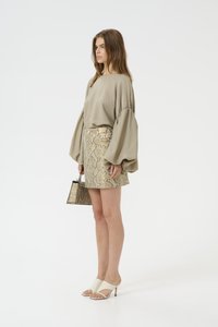Blusa beige con maniche a palloncino, mini gonna a motivo serpente, mules bianche con tacco, accessoriata con una piccola borsa a tracolla con stampa di serpente.