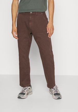 Brown cotton pants with a relaxed fit and visible front pockets. The fabric features subtle texture, complemented by gray sneakers.