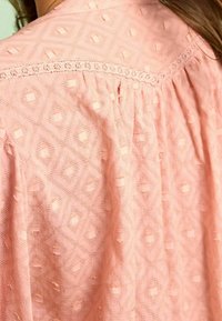 Top in cotone rosa con un motivo a diamante testurizzato, merlettatura dettagliata lungo le spalle e tessuto arricciato per una vestibilità rilassata.
