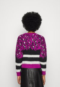 Knit sweater featuring a vibrant pink leopard pattern, black and white striped accents, and a cropped design with a soft texture.