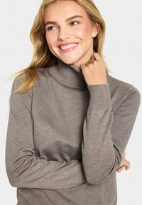 Světle hnědý rolák se žebrovanými manžetami a límcem, vyrobený z měkké, strukturované tkaniny, s přiléhavým střihem.