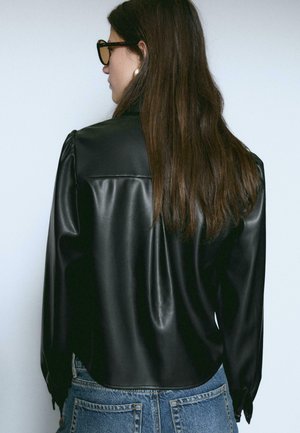 Schwarze Kunstlederbluse mit langen Ärmeln, gerafftem Schulterdetail und glatter Textur, kombiniert mit hochtaillierten Jeans.