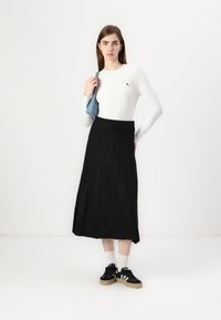 Lett hvit langermet topp med liten logo, sammen med en luftig svart pregget skjørt og svarte sneakers med hvite striper.
