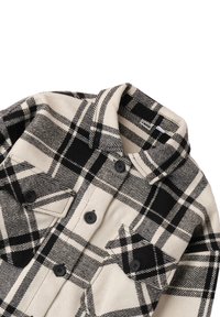 Black and white plaid flannel shirt featuring a collar, button closures, and two chest pockets. Soft texture with prominent grid pattern.