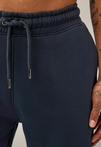 Joggers azul marino hechos de una tela suave, que cuentan con una cinturilla elástica, cordón con terminales de metal plateado y una textura suave.
