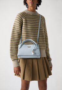 Borsa a mano blu chiaro dalla forma strutturata, superficie testurizzata e manici superiori. Presenta un piccolo charm e dettagli metallici. Indossata a tracolla.