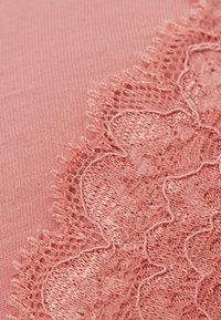 Jasnoróżowa tkanina z misternymi koronkowymi detalami wzdłuż krawędzi, o falistym wzorze i teksturowanej powierzchni.