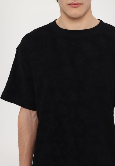 Chemise noire à manches courtes avec un motif floral texturé, col rond et tissu doux. Présente une coupe ample et des détails de design minimalistes.
