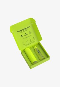 Det ljusgröna förpackningen innehåller två produkter: en cylindrisk solkrämsflaska och en matchande strukturerad sprayflaska. Lådan har produktinformation.