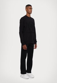 Sort sweatshirt med præget logo, bådudskæring og ribbede manchetter, parret med sorte jeans og hvide sneakers for et monokromt look.