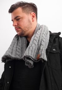 Gray knitted scarf with a cable pattern, featuring a leather accent. Worn loosely around the neck, displaying texture and thickness.