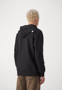 Czarna bluza z kapturem wykonana z miękkiego materiału, z logo na górnej części pleców. Żebrowane mankiety i dół oraz luźny krój.