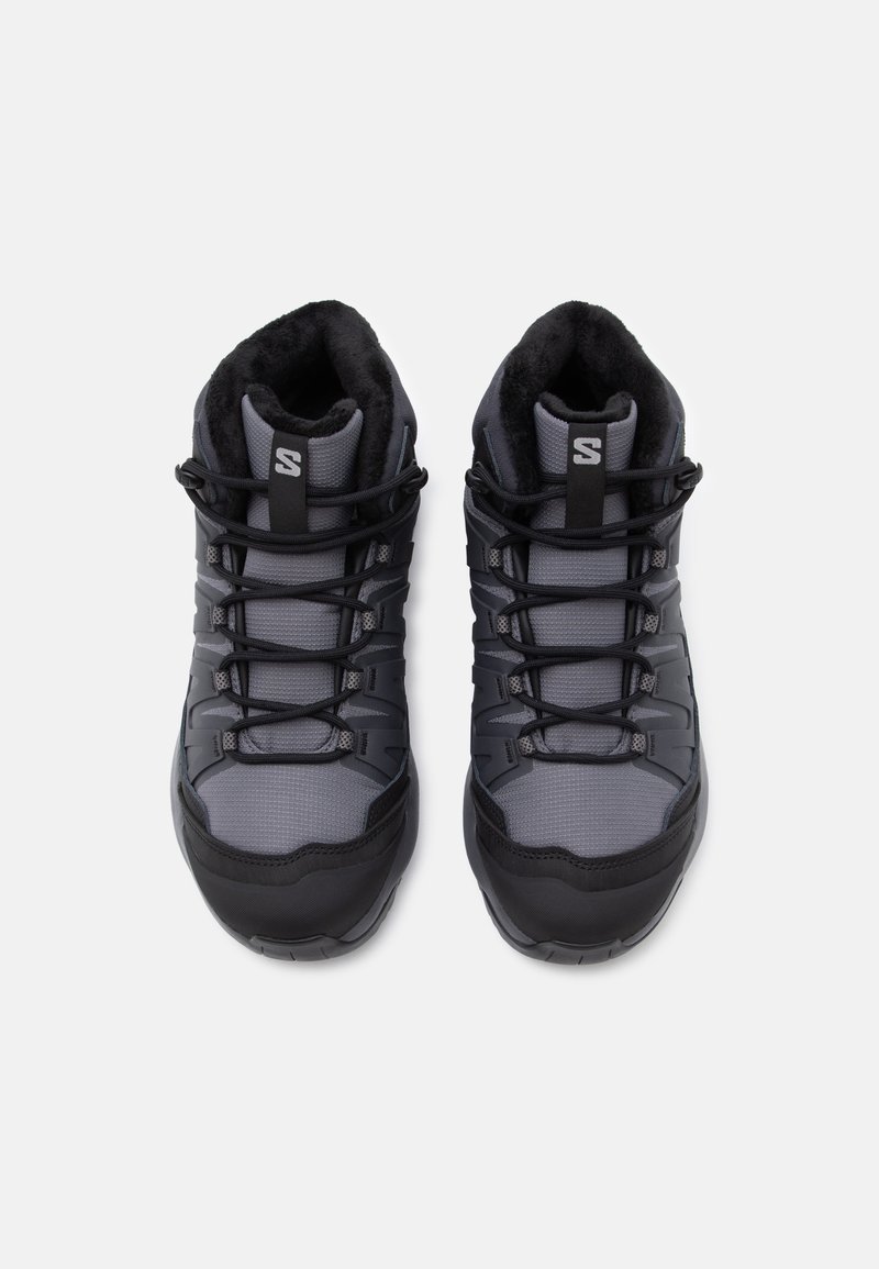 Scarponi da trekking grigi con parte superiore in rete testurizzata, suole in gomma nera e lacci elastici. Presentano un collare imbottito e accenti con logo.