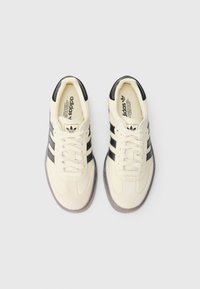 Tenisky krémové barvy s černými pruhy a detaily, disponující gumovou podrážkou, šněrovacím designem a texturovanými překrytími.