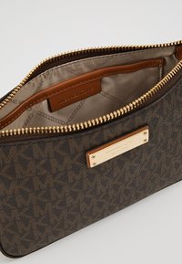 Bruine leren pouch met een patroon, voorzien van een gouden rits en een metalen logo plaatje. De zachte, gevoerde binnenkant heeft een tan leren label.