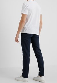Camiseta blanca de manga corta y pantalones marinos de corte recto, combinados con zapatillas blancas. Diseño sencillo y colores sólidos.
