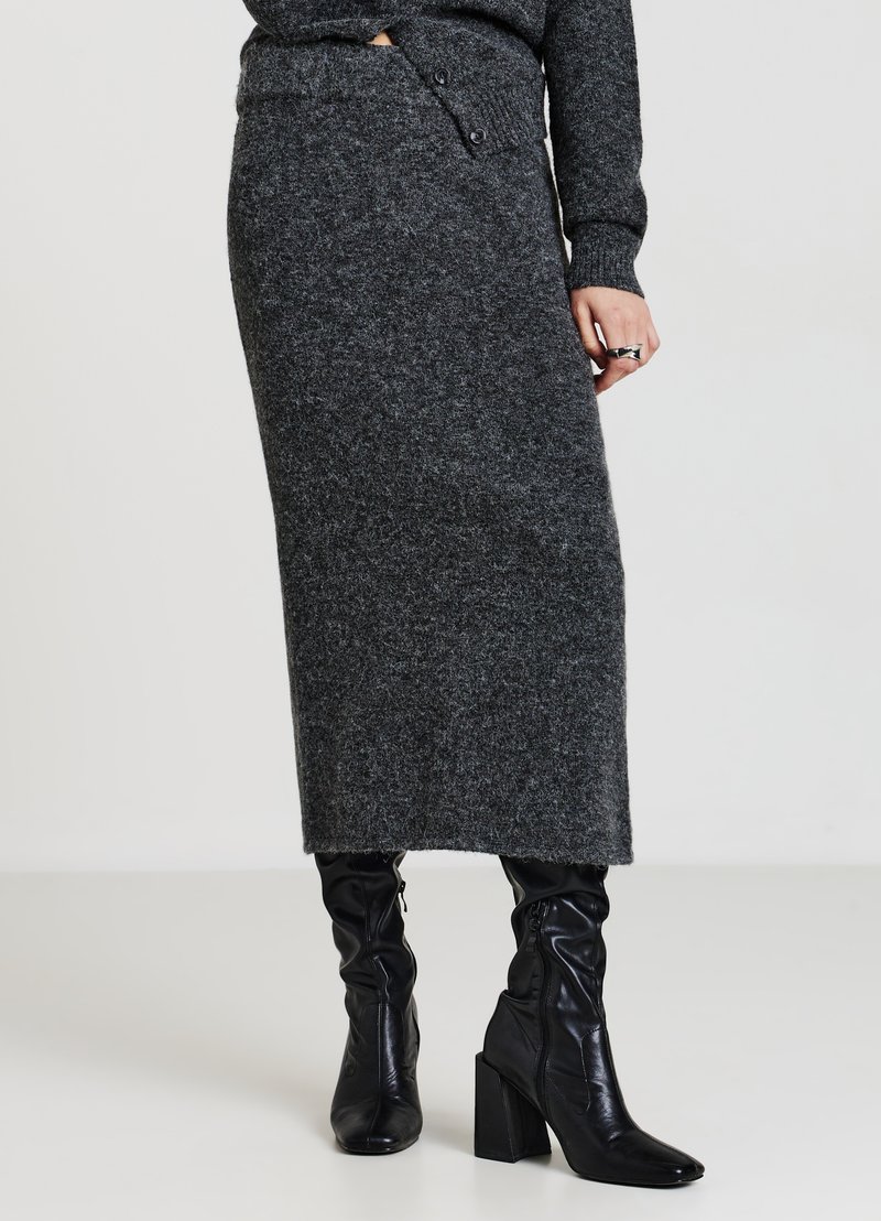 Jupe midi gris en mélange de laine avec une taille haute, des boutons latéraux et une finition douce et texturée, associée à des bottes noires à talons mi-hautes jusqu'aux genoux.