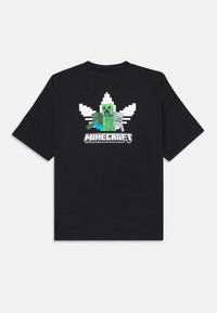 T-shirt nera a maniche corte con un graffito pixelato di un creeper verde e uno scheletro sulla schiena, accompagnato da una foglia bianca e dal testo "MINECRAFT".