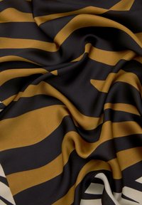 Hedvábný šátek s výraznými vlnitými pruhy v černé a zlaté barvě na krémovém pozadí, s hladkým povrchem a složitým drapováním.