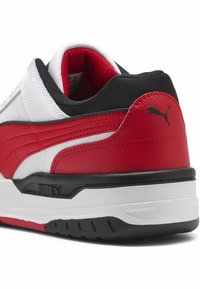 Sneakers Puma w kolorach białym, czerwonym i czarnym. Charakteryzują się teksturowaną skórzaną cholewką, wyściełanym kołnierzem oraz gumową podeszwą z akcentami logo.