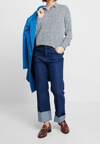 Hemd mit hellblauen und weißen Muster, dunkle Jeans mit umgeschlagenen hellblauen Bündchen und braune Loafer, kombiniert mit einem blauen Blazer.