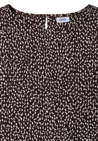 Blouse marron à motif abstrait de pois blancs, encolure ronde, petite goutte dans le dos et étiquette en tissu visible portant l'inscription "Cecil."
