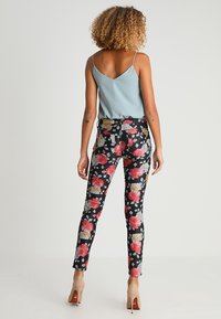 Schwarze Stretch-Hose mit floralen Druck, rosa und gelbe Rosen. Kombiniert mit einem hellblauen, ärmellosen Oberteil. Glattes Material, taillierte Passform.