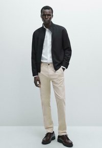Black jacket, white shirt, beige pants, and brown shoes. Slim fit, cotton material, with a smooth texture and subtle accents.