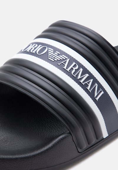 Μαύρο σανδάλι σαγιονάρας με υφή στη σόλα και λευκή ρίγα που φέρει το λογότυπο Emporio Armani και το έμβλημα με το αετό στο λουράκι.