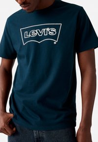 T-shirt en coton bleu marine avec un logo Levi's blanc en contour arrondi. Manches courtes et col rond. Design minimaliste.