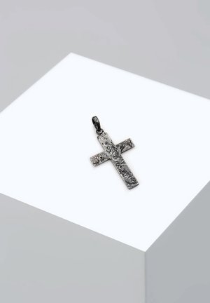 Ciondolo a forma di croce in metallo con una finitura nera opaca e texture, caratterizzato da un design geometrico semplice con un anello per il fissaggio, esposto su un piedistallo bianco.