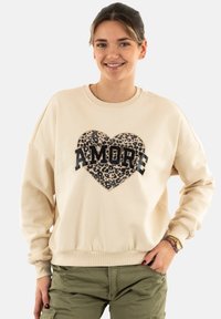 Sudadera beige con un gran corazón de estampado de leopardo y texto negro "AMORE". Presenta puños y dobladillo acanalados, corte relajado y textura suave.