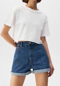Camiseta blanca corta de manga corta combinada con pantalones cortos de mezclilla de tiro alto con dobladillos enrollados y cierre frontal de botón.