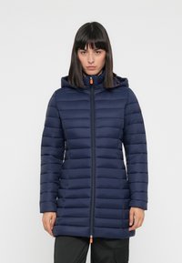 Navy pufferjack met horizontale stiksels, ritssluiting aan de voorkant en een verstelbare capuchon. Kenmerkend zijn de oranje accenten en het slanke, verlengde ontwerp.